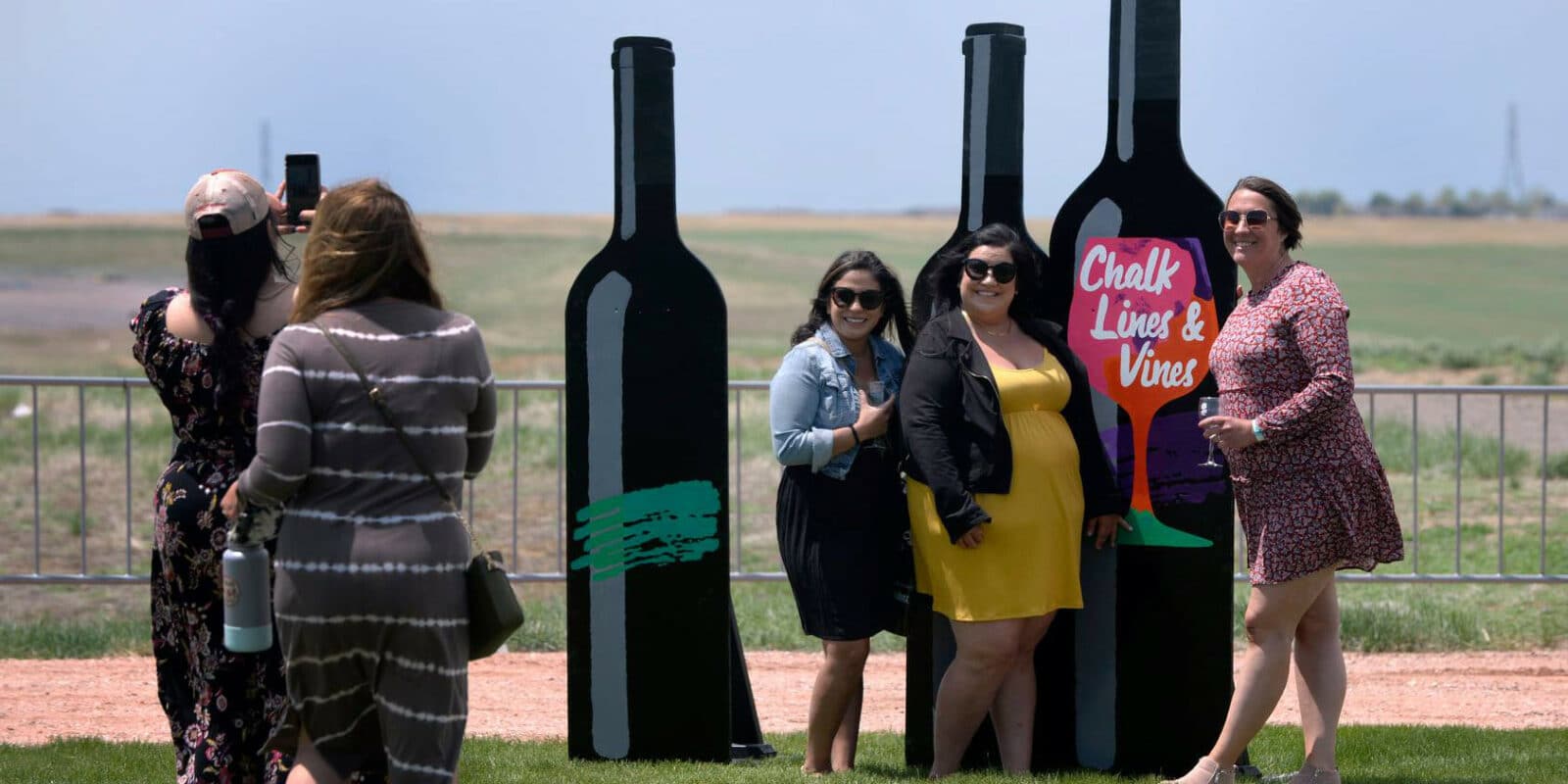 Three guests at the Chalk Lines and Vines Festival in Aurora posing in front of blow-up wine bottles for a picture.