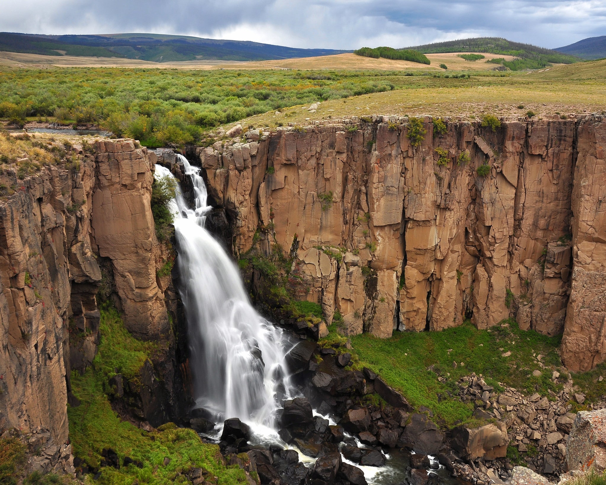 Rolling grass hills with sudden brown rockface and large flowing North Clear Creek waterfall. 