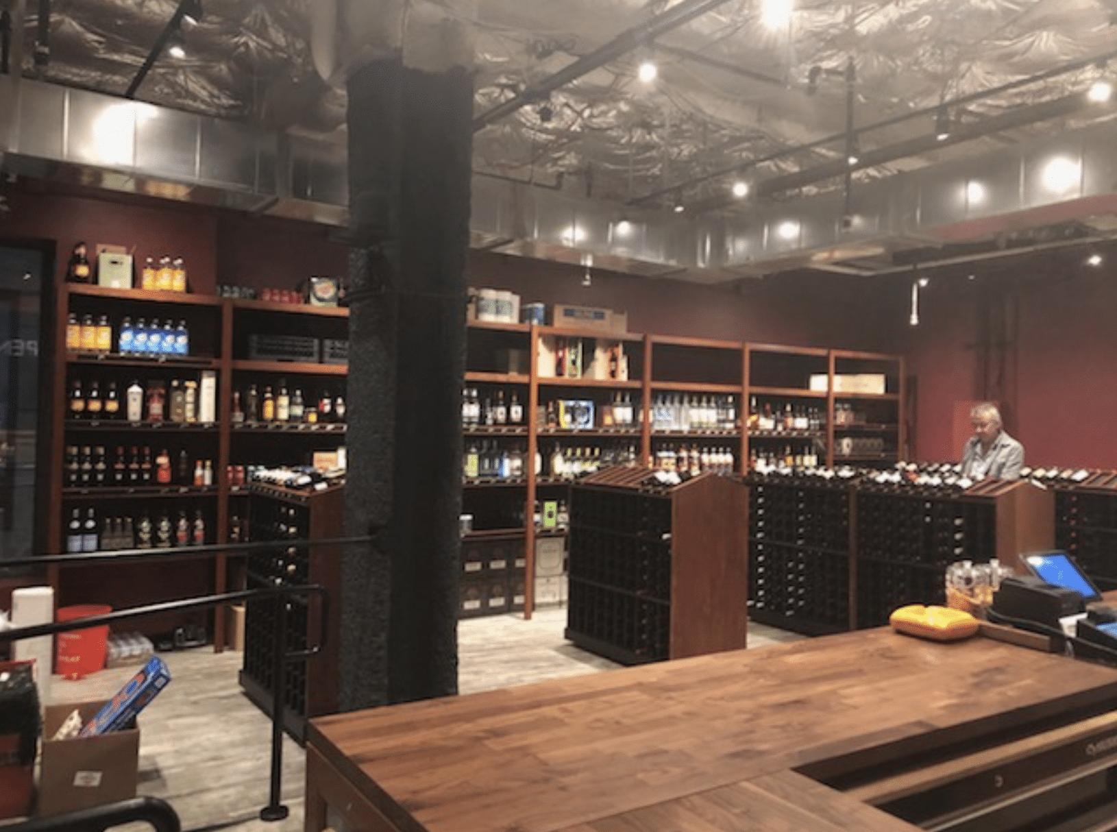 Interior of Denver Wine Dispensary with several dark wooden shelves of wine and a person browsing