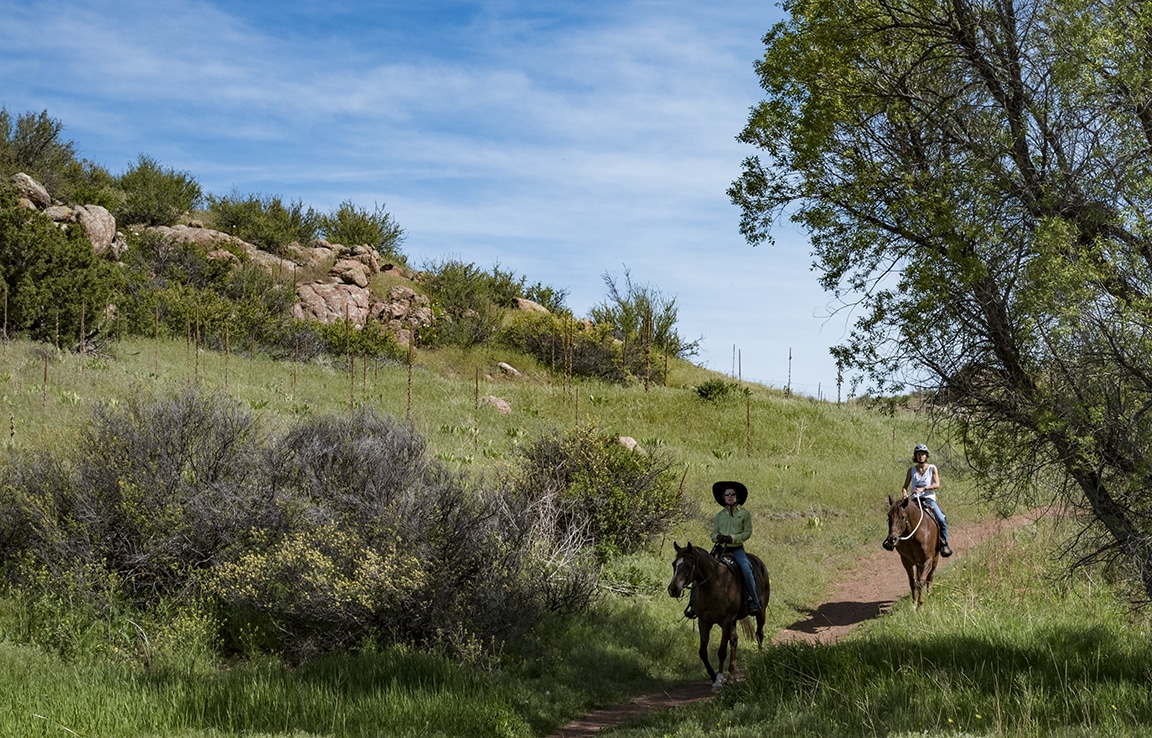 Two people on horseback riding through the hilly, green Eagle's Nest Open Space