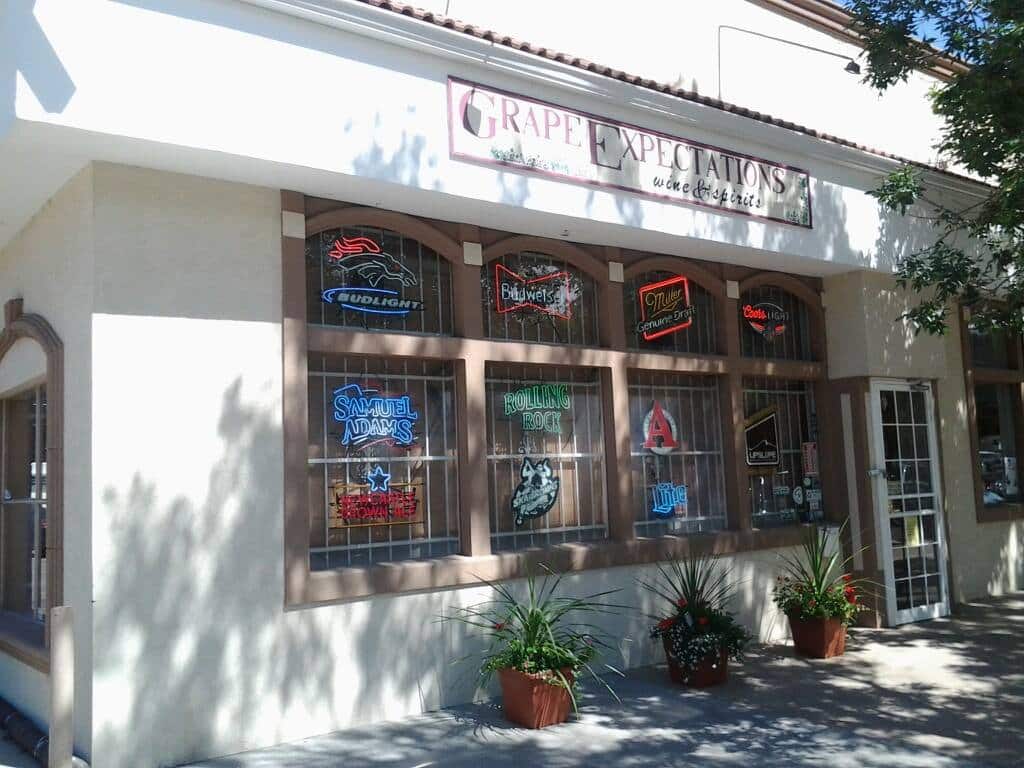 Storefront of Grape Expectations Wine & Spirits in Denver. White building with a few windows featuring popular alcohol brand decals