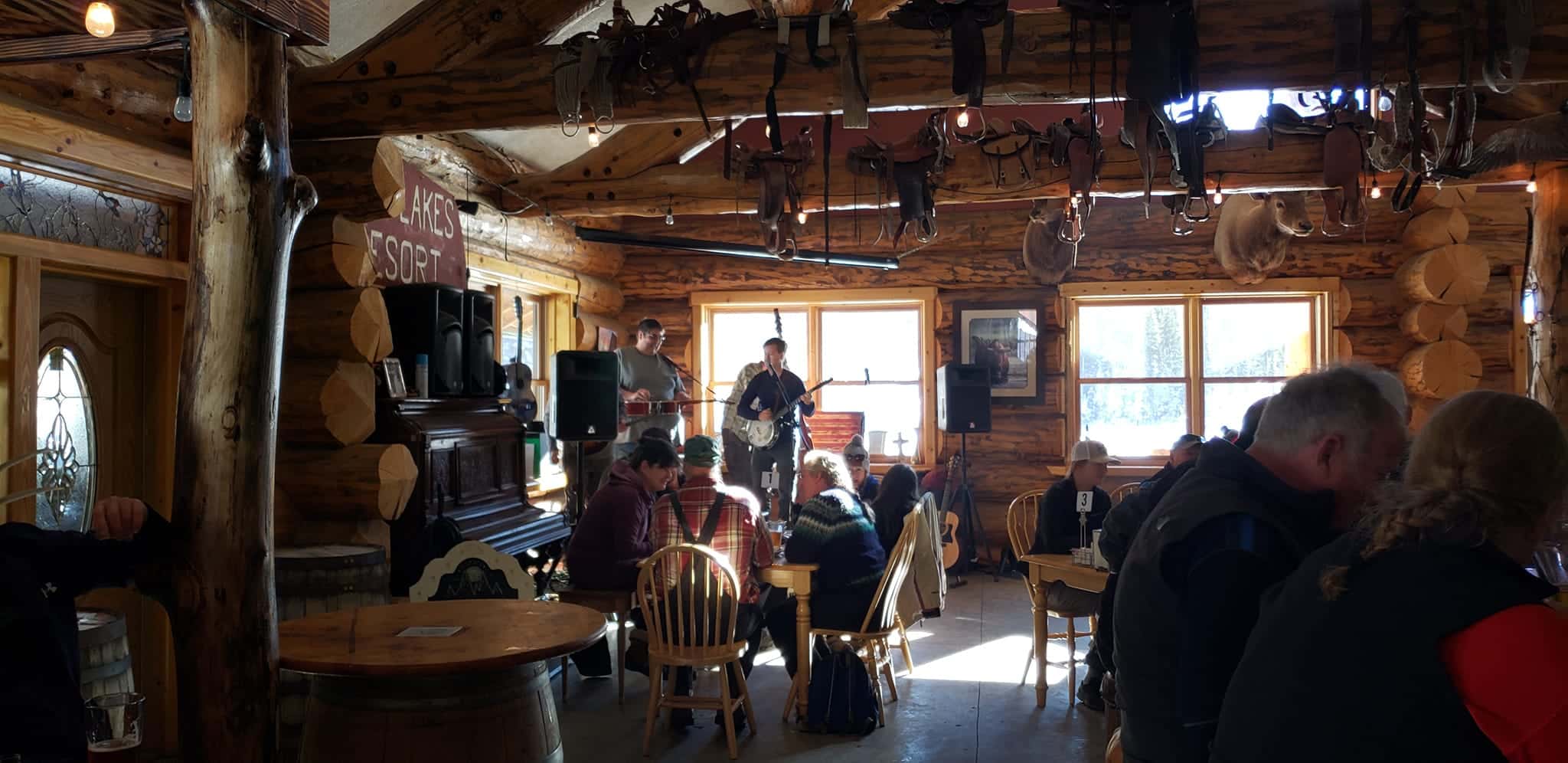 Dining area in a wooden lodge at the restaurant in Mesa Lakes Lodge. Vaulted wooden ceilings over a room full of people gathered around tables enjoying a meal and listening to a live band perform