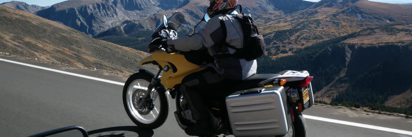 Motorcycle rider on yellow bike cruising along a high elevation road in Rocky Mountain National Park in central Colorado