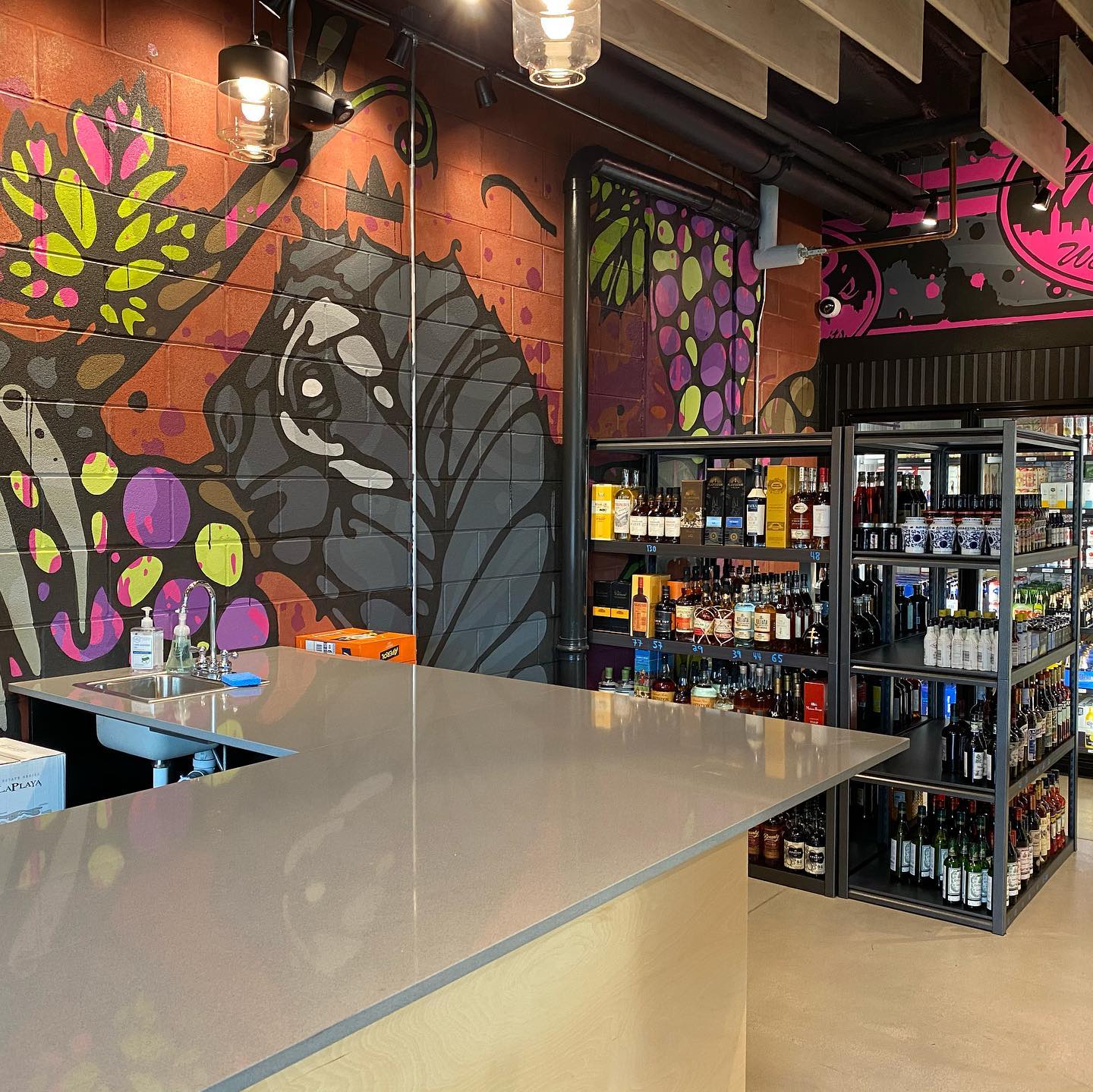 Checkout counter at Mr. B's Wine & Spirits in the Golden Triangle neighborhood of Denver. Colorful, eccentric mural on the back wall and several black, boxy racks of wine to the right