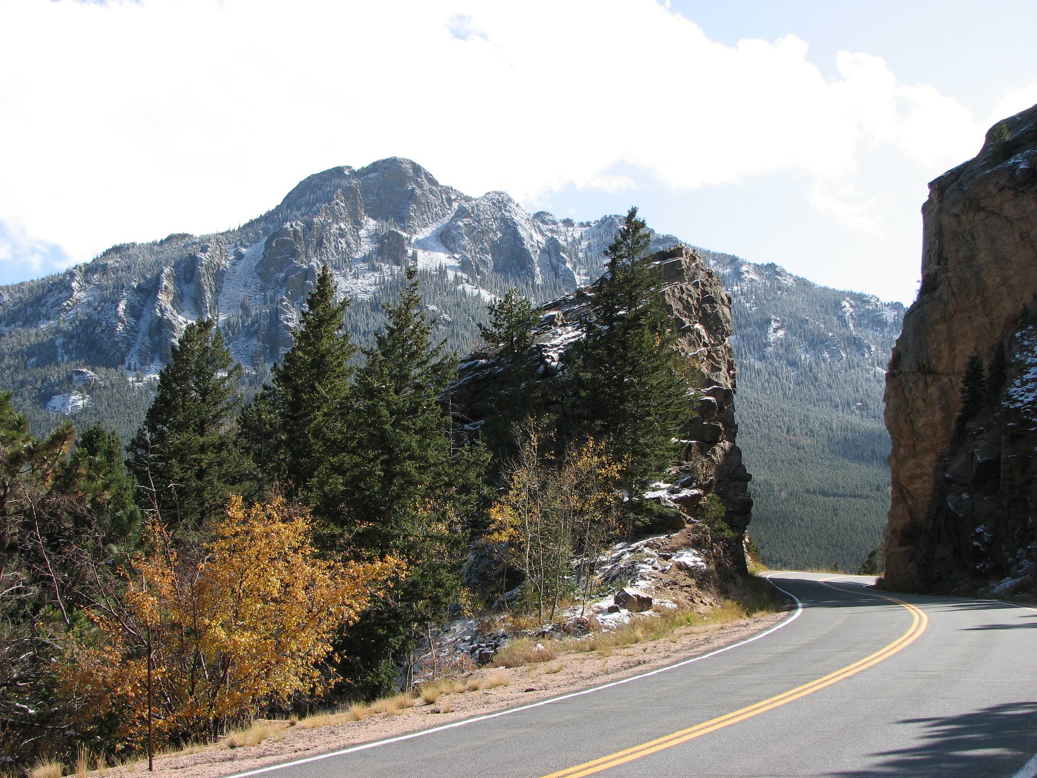 Road disappearing around the corner on the Peak to Peak Byway, connecting Estes Park to Black Hawk. Mountains in background