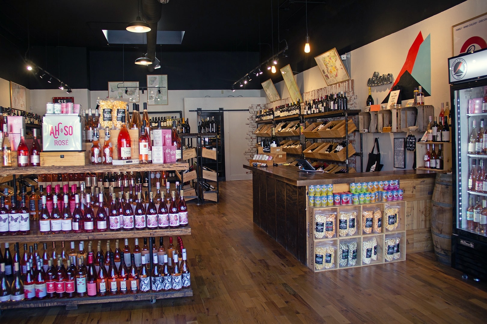 Interior of Pearl Wine Company's location in Denver's Platt Park neighborhood. Several wooden shelves of wine and a rose display front and center. 