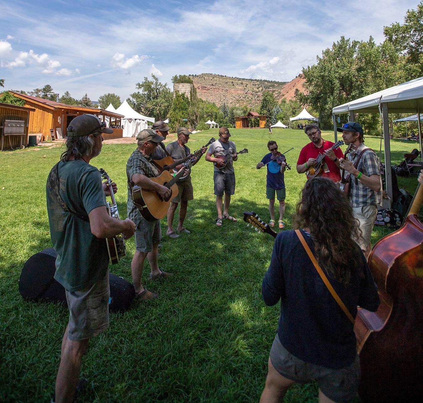 Circle of people at RockyGrass bluegrass festival in Lyons playing guitars on a grassy field. 