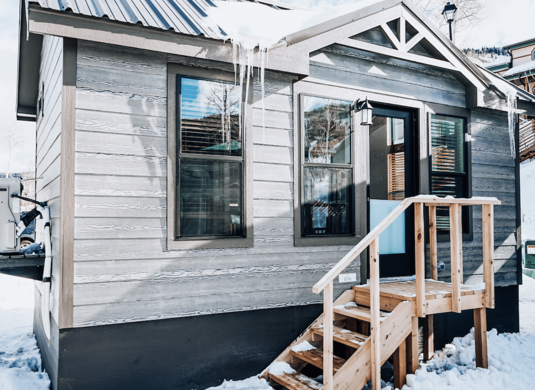 Exterior of a tiny home at Powderhorn Mountain Resort in Mesa. Small grey building with a few windows and a small staircase leading down from the front door. 