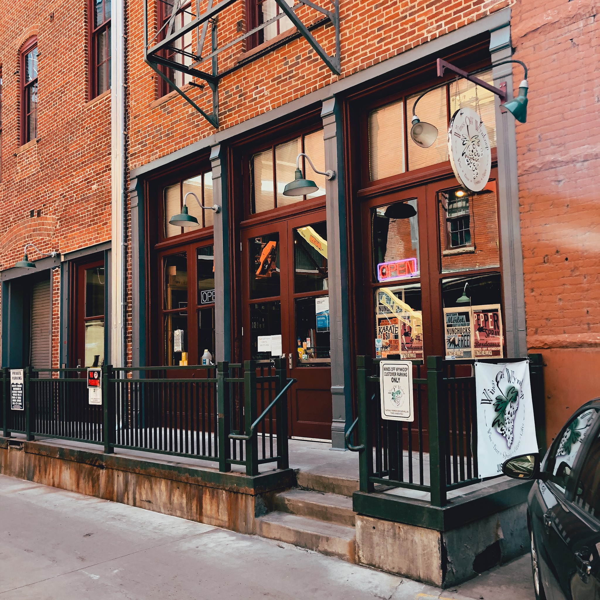 Storefront of Wines Off Wynkoop in Denver. Red brick building with large wooden windows and doors with a small patio area. 