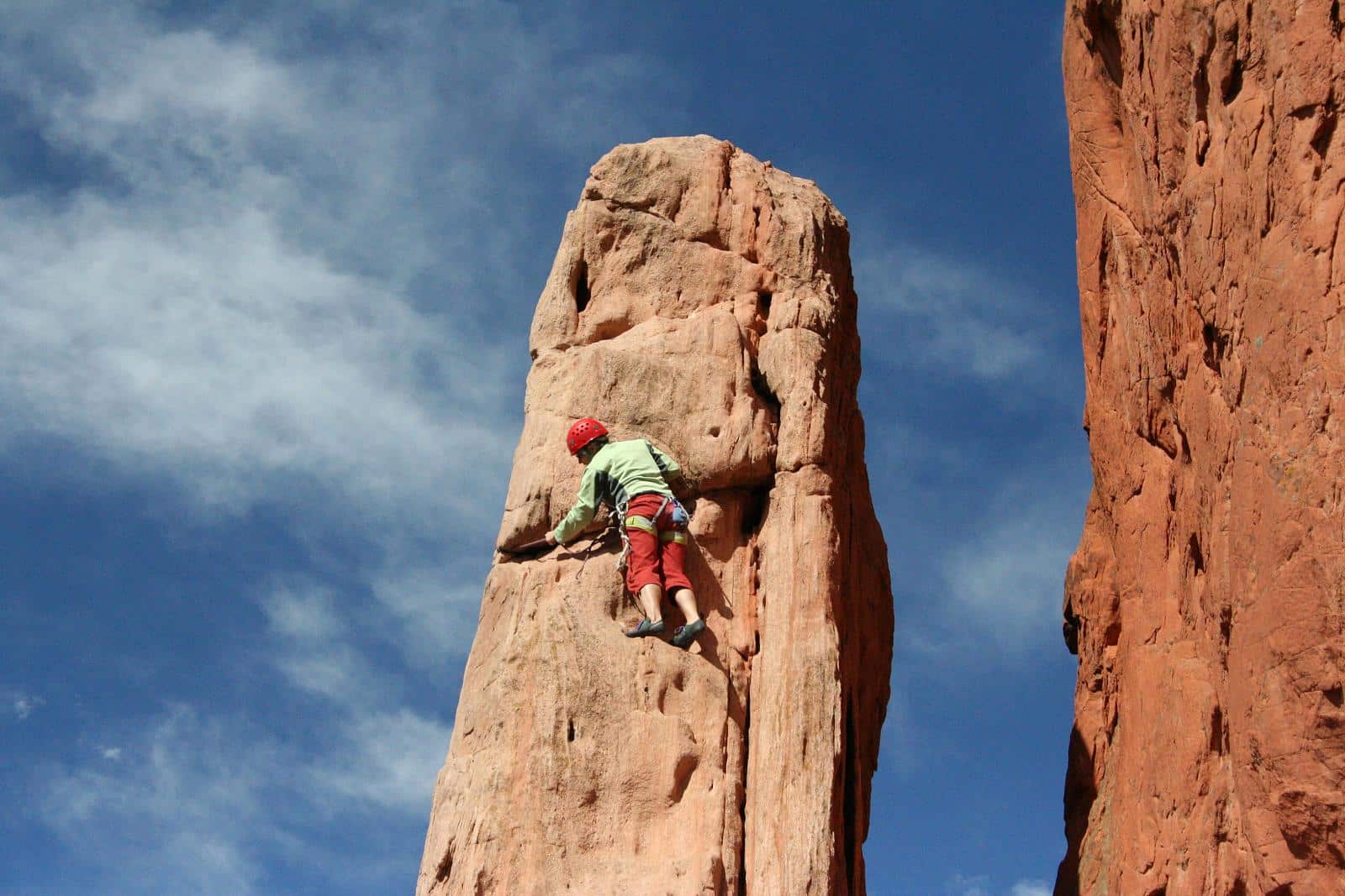 Climber in green top and red pants climbing up a lone red rock spire at Garden of the Gods near Colorado Springs