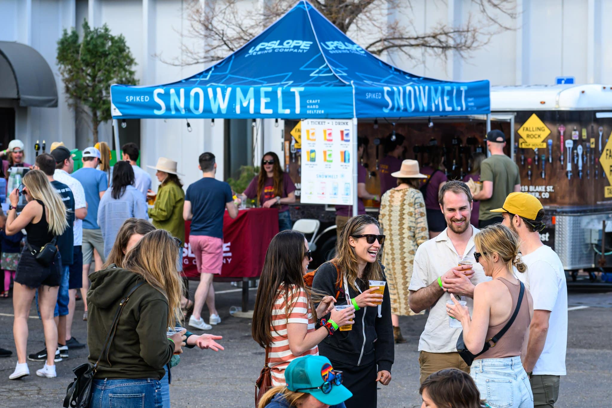 People gathered around a large blue Upslope Brewing Tent in Boulder. Most people are laughing and holding plastic cups of beer