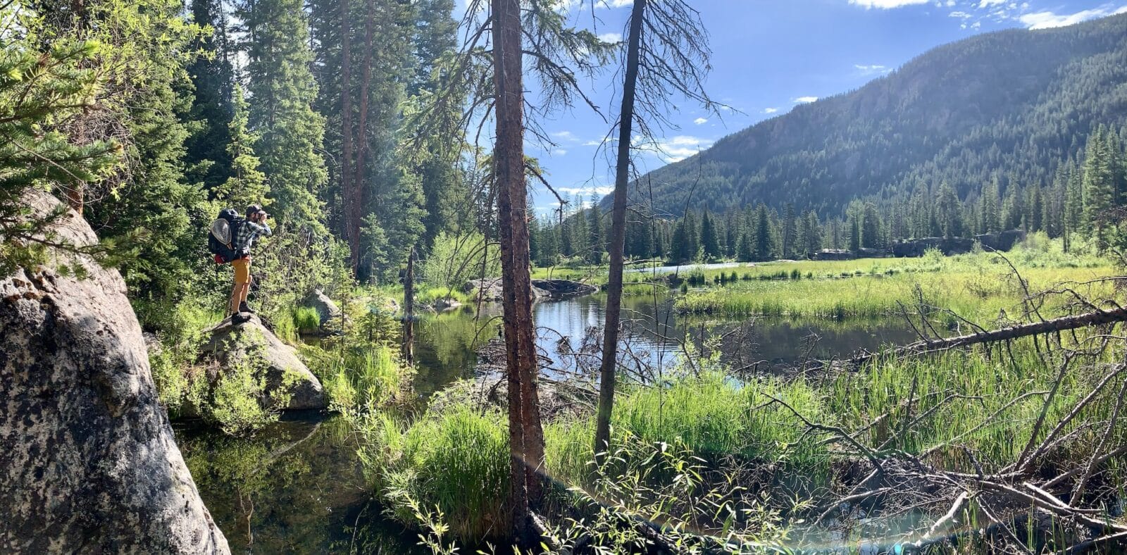 fisherman stands on shores of Surprise Lake pointing a camera near Vail, Colorado
