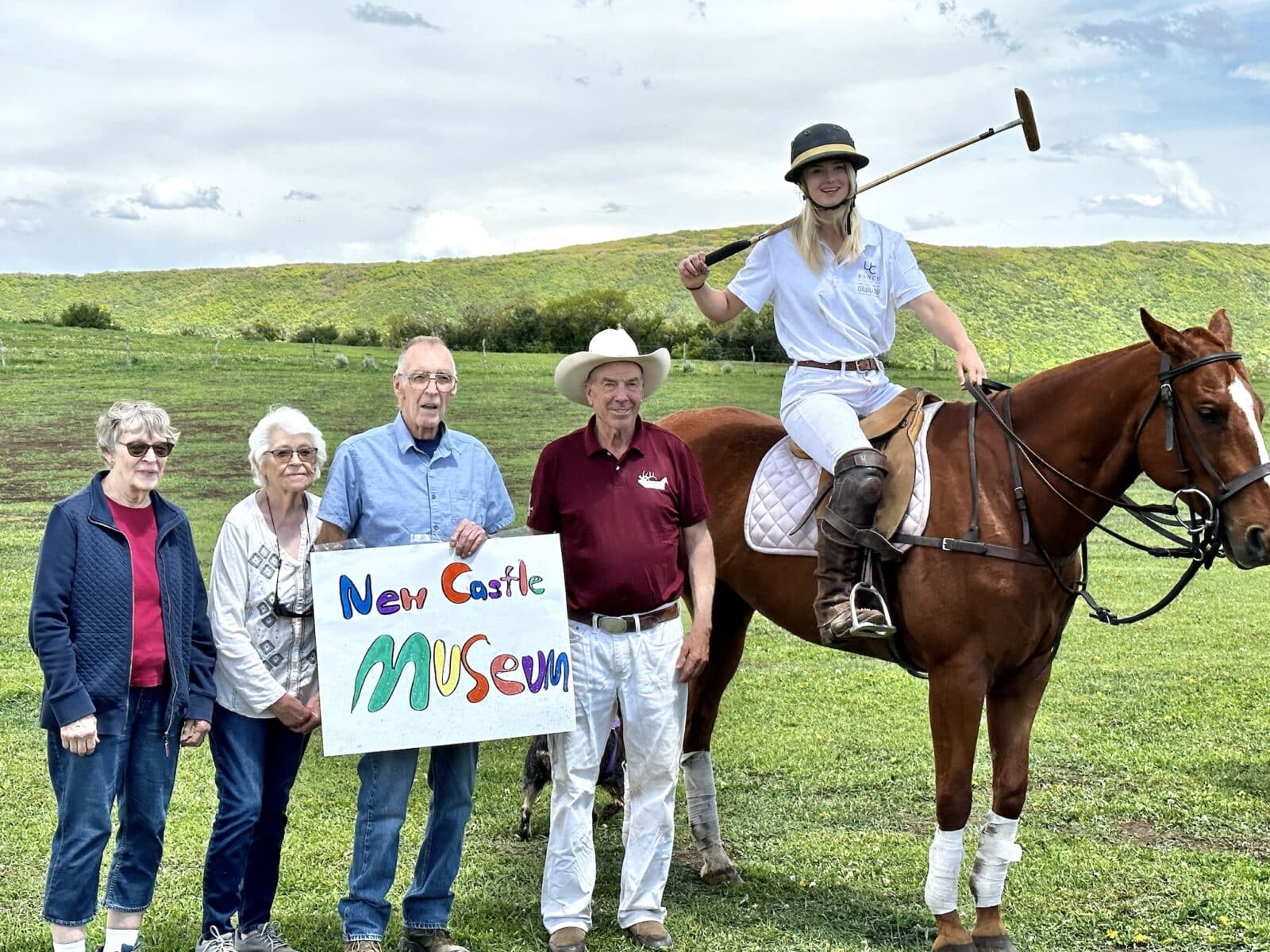 Woman polo player on horse with people standing holding a sign for the New Castle Museum