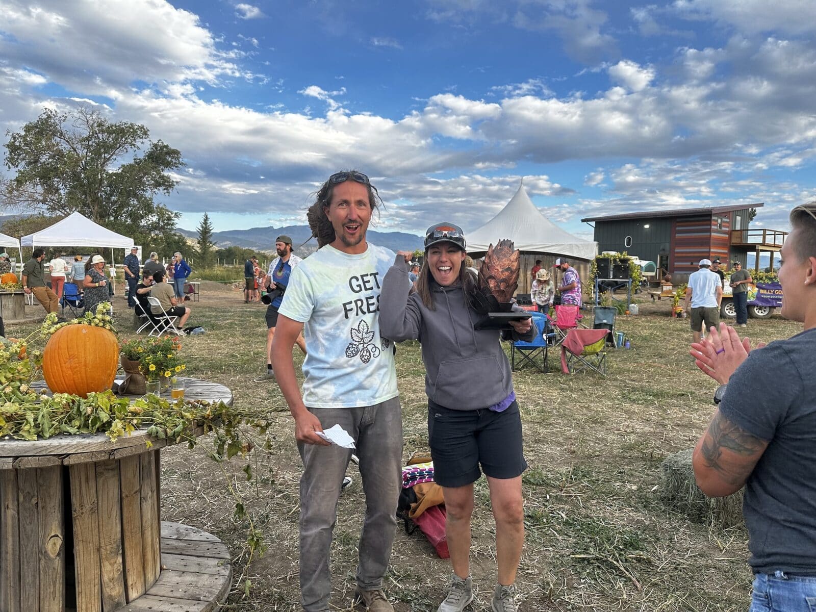 woman holds a trophy that looks like big bronze hops and poses with man for picture at Billy Goat Hop Farm