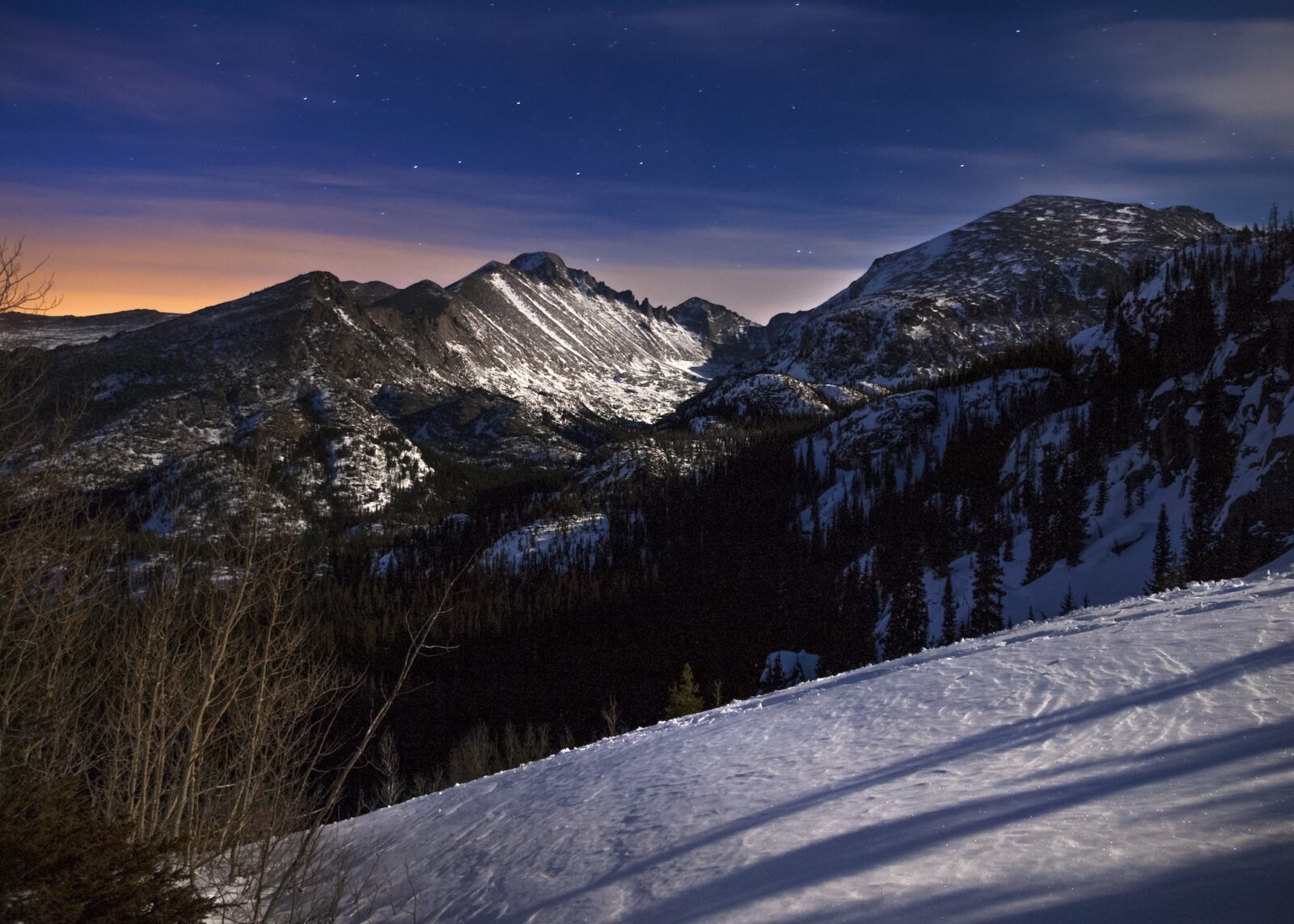 Winter day with snow at night lit up by the moon with some stars visible