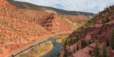 Rocky Mountaineer train rolls along in a red rock canyon by the river