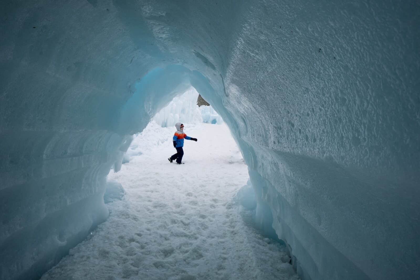 kid walks by a tunnel made of ice at Ice Castles