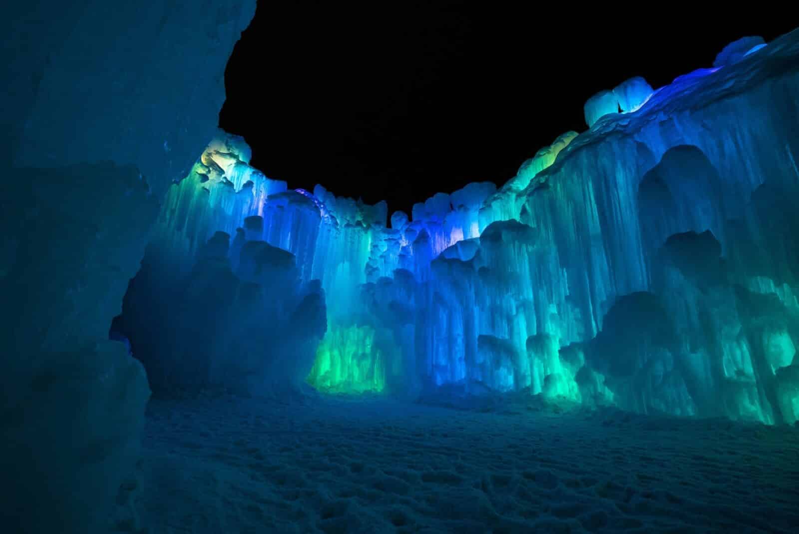 large ice castles lit up at night with blue and green in Colorado