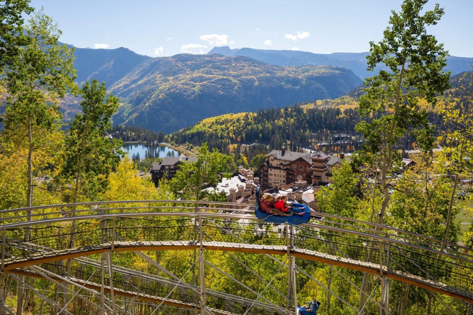 two girls in one mountain coaster car ride down the hill overlooking fall colors and Purgatory Resort