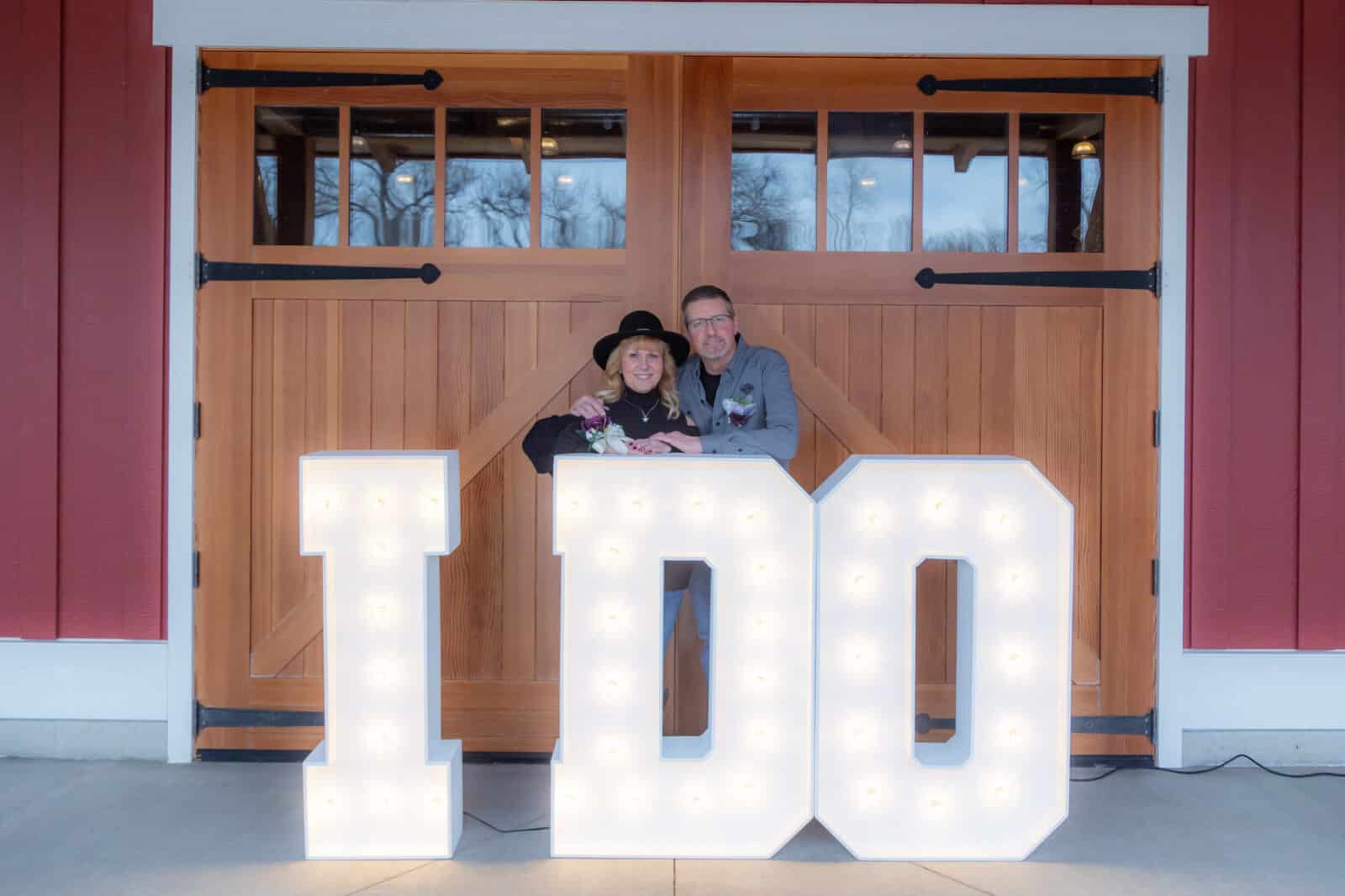 couple stands outside behind a large "I DO" light up sign at the Loveland Valentine's Day Group Wedding