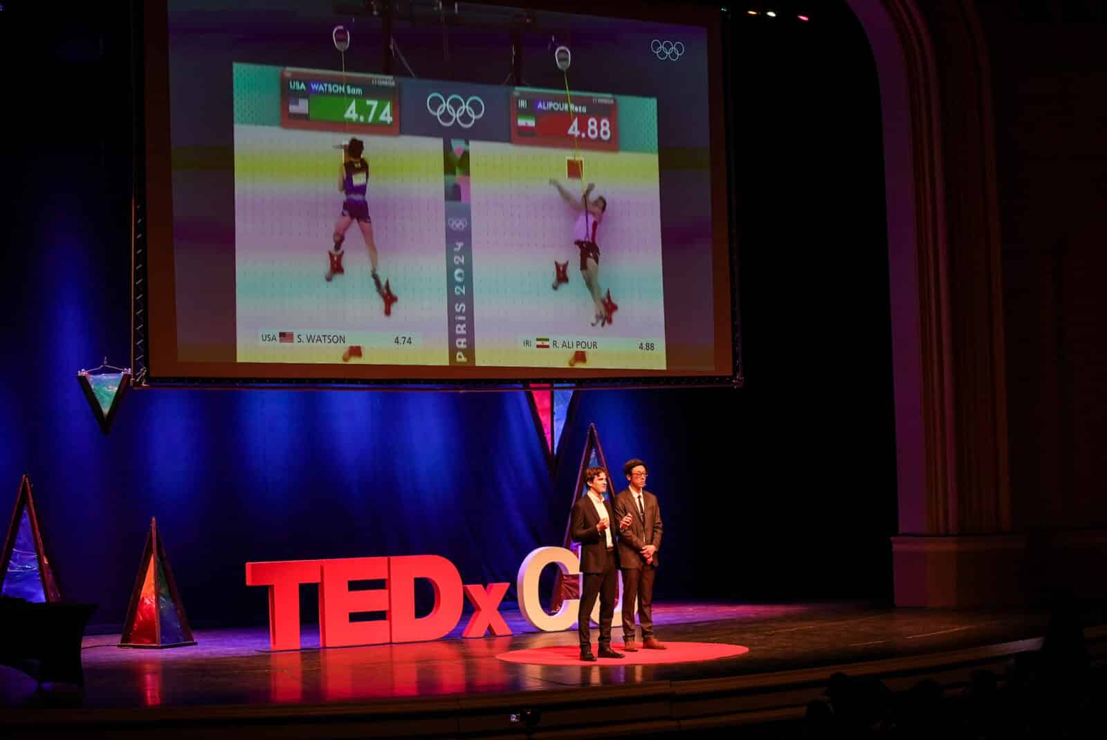 two men speak on stage at TEDxCU