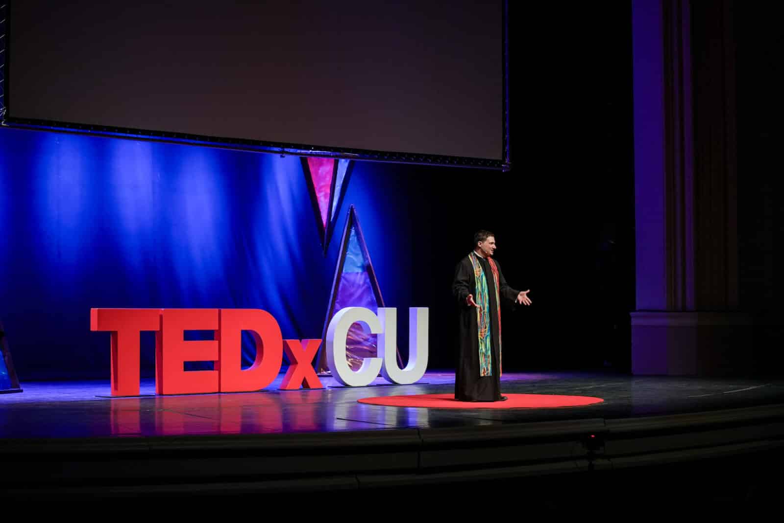 man speaks on stage at TEDxCU